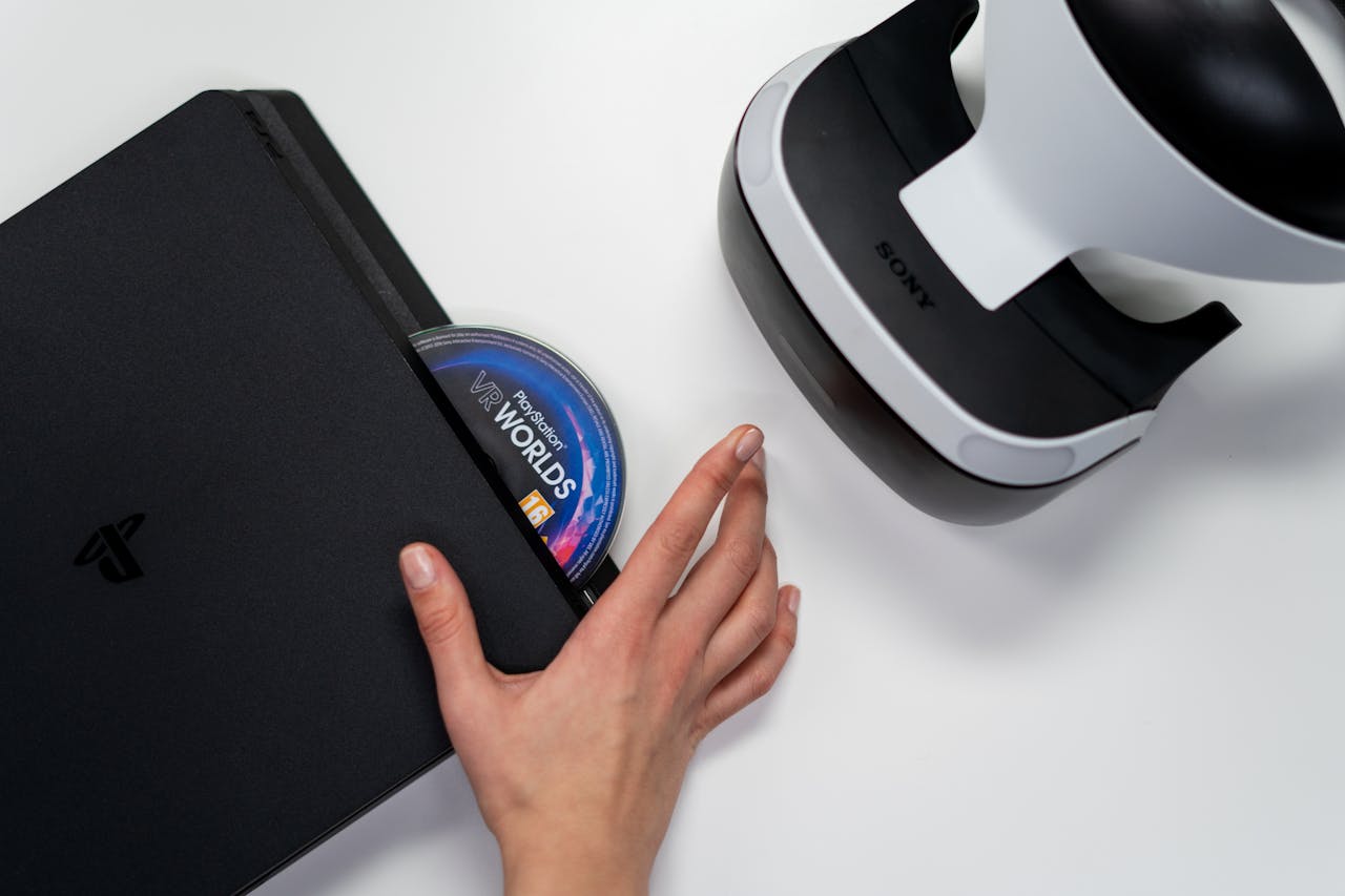 Close-up of a hand inserting a VR Worlds disc into a PlayStation with VR headset nearby.